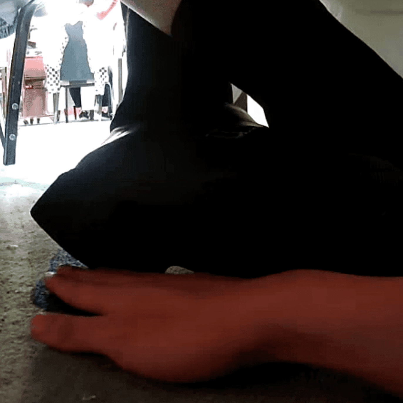 Girl candid steps on hand with her cute black leather shoes under the table
