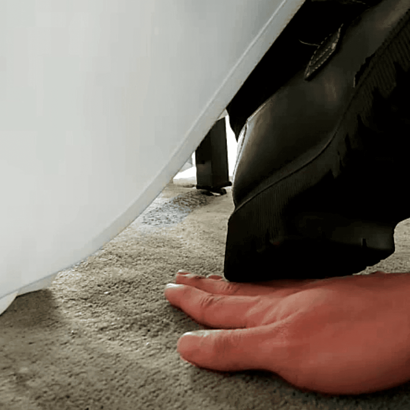 Girl candid steps on hand with her cute black leather shoes under the table