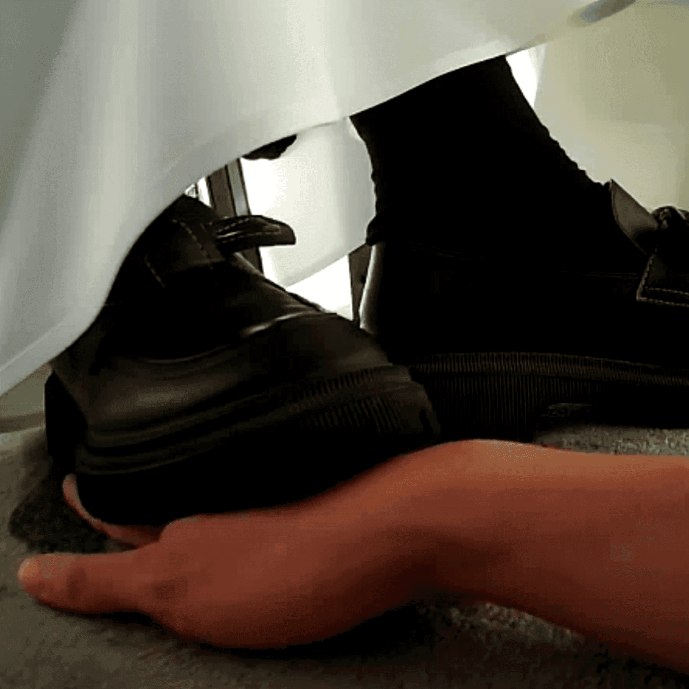 Girl candid steps on hand with her cute black leather shoes under the table